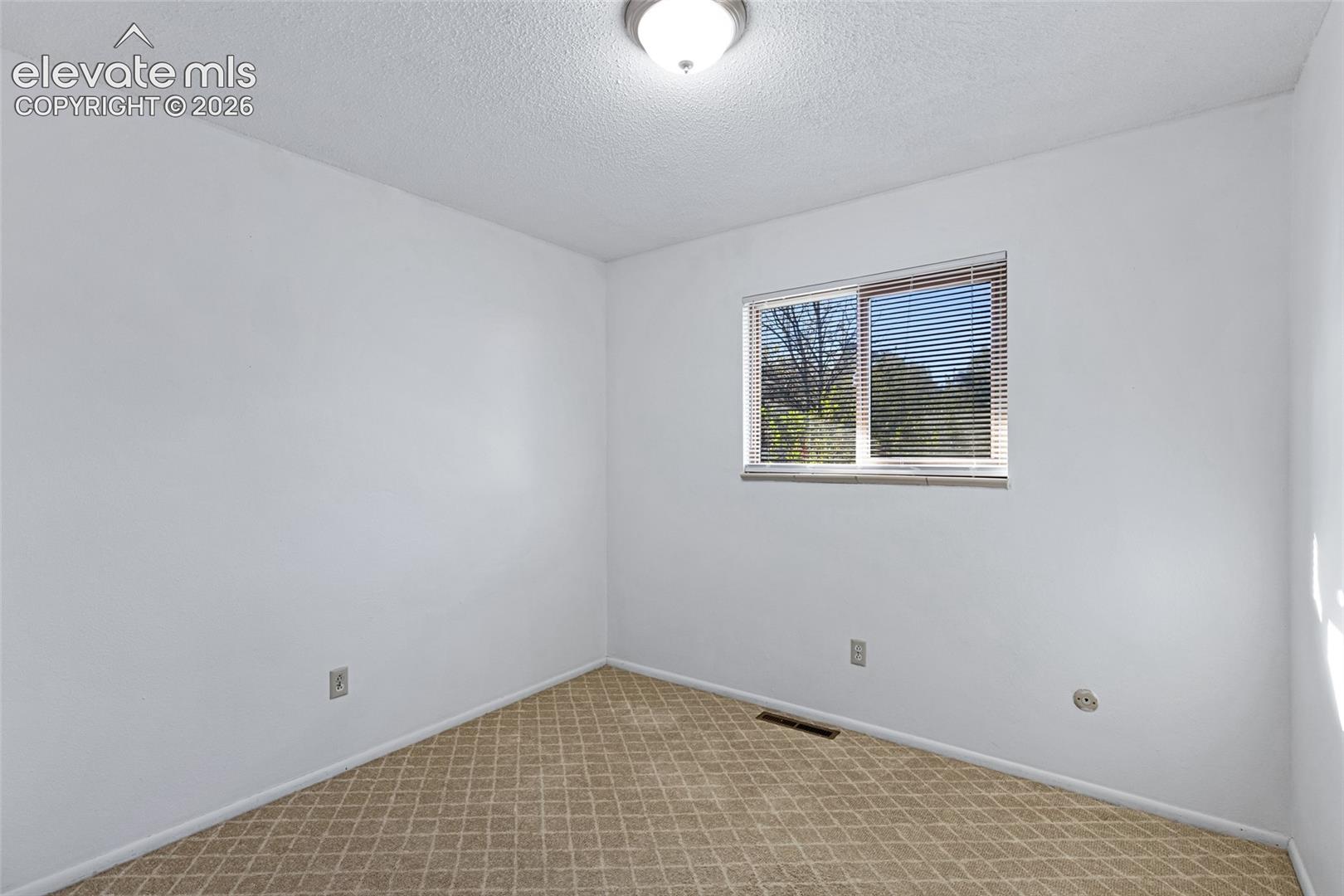 Bright corner bedroom with natural light from dual-pane window, neutral white walls, and patterned tile flooring
