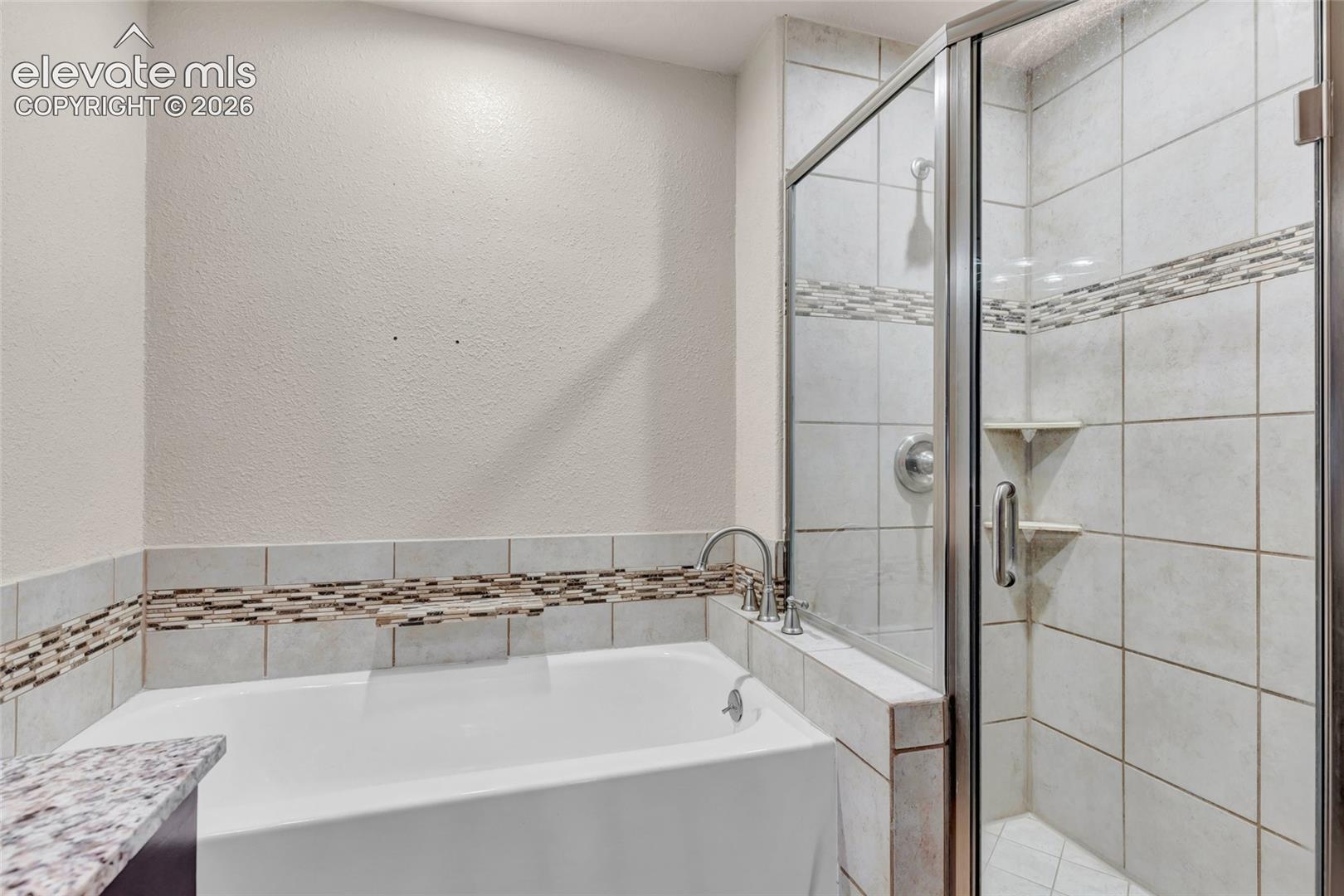 Soaking tub with deck-mounted faucet, complemented by a tiled shower enclosure featuring a glass door and integrated shelving