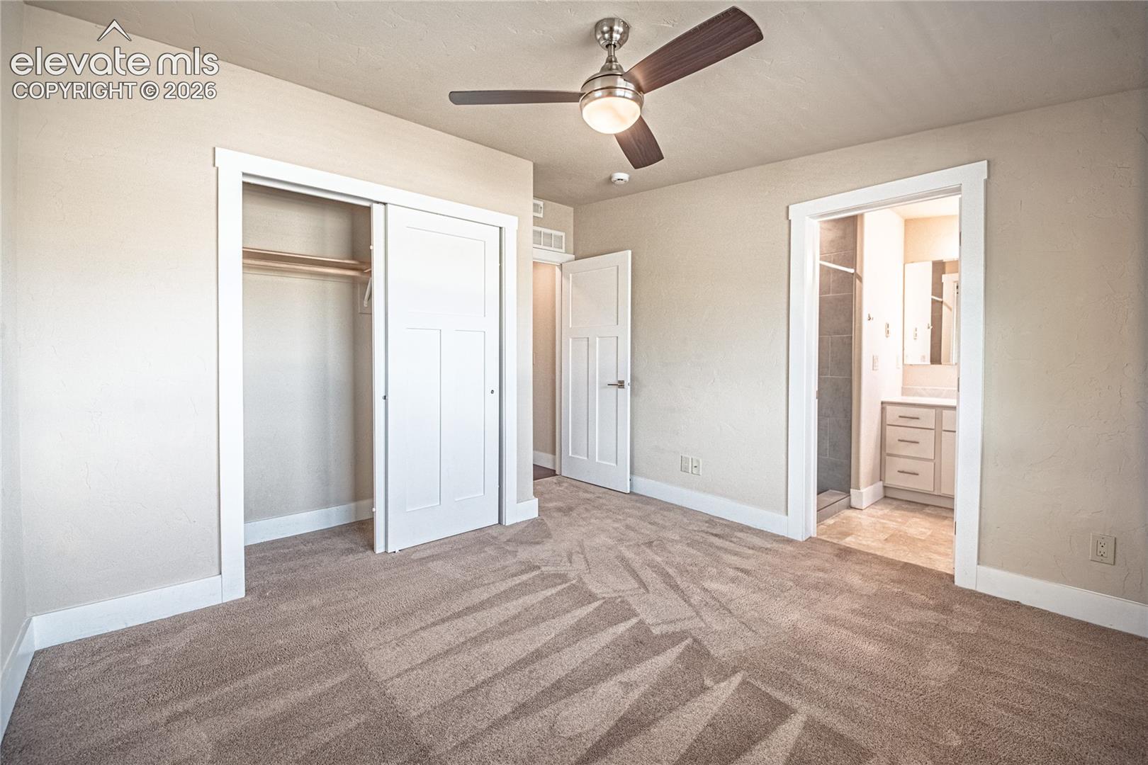 Carpeted room with a ceiling fan, featuring a sliding closet door and an entry to an attached bathroom