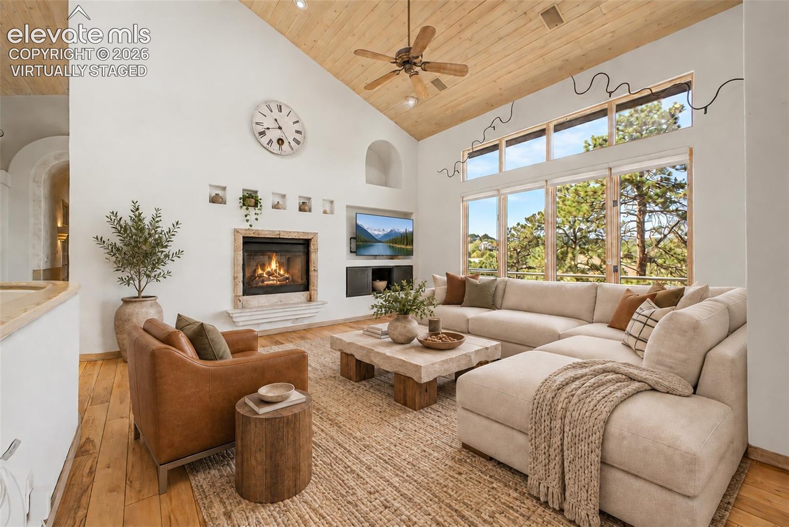 Virtually Staged
Vaulted wood-paneled ceiling with a ceiling fan, a stone fireplace, large picture windows, wood-finish flooring, and arched wall alcoves