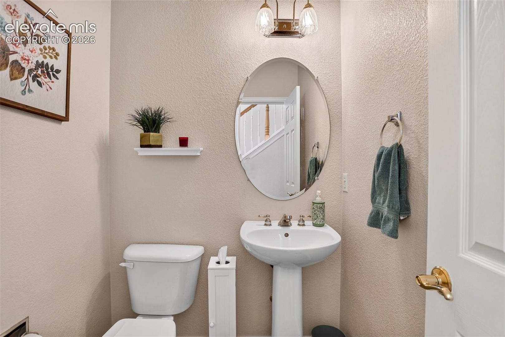 Pedestal sink with dual-handle faucet, oval mirror, wall-mounted light fixture, and white toilet
