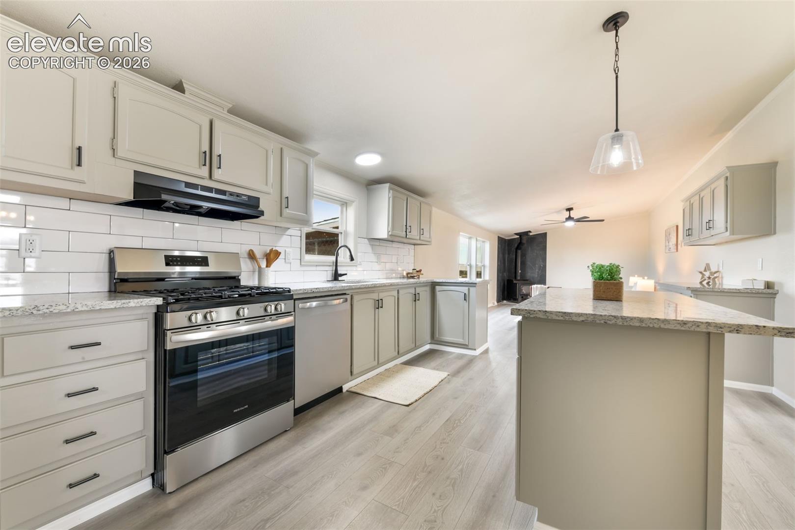 Kitchen featuring light gray cabinetry, white subway tile backsplash, stainless steel appliances, light-toned countertops, and wood-finish flooring