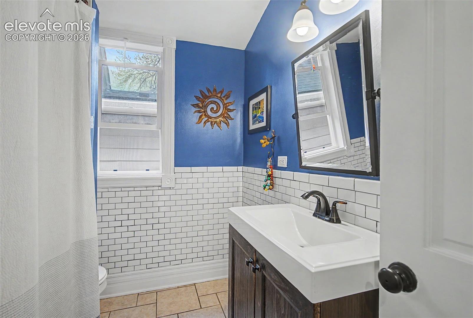 3/4 Bathroom on main level featuring white tiling, a dark wood-finish vanity with an integrated white sink, and ceramic tiling