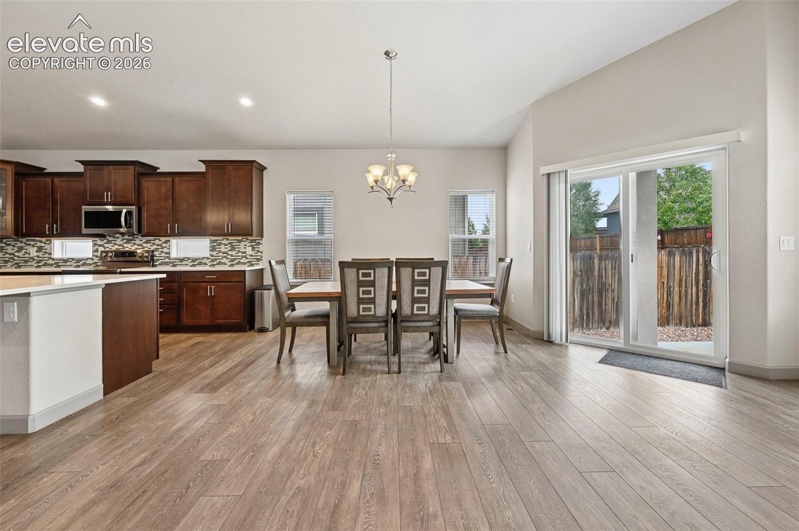 Open-concept interior featuring wood-finish flooring, dark-toned cabinetry, a mosaic tile backsplash, a tiered chandelier, and sliding glass doors