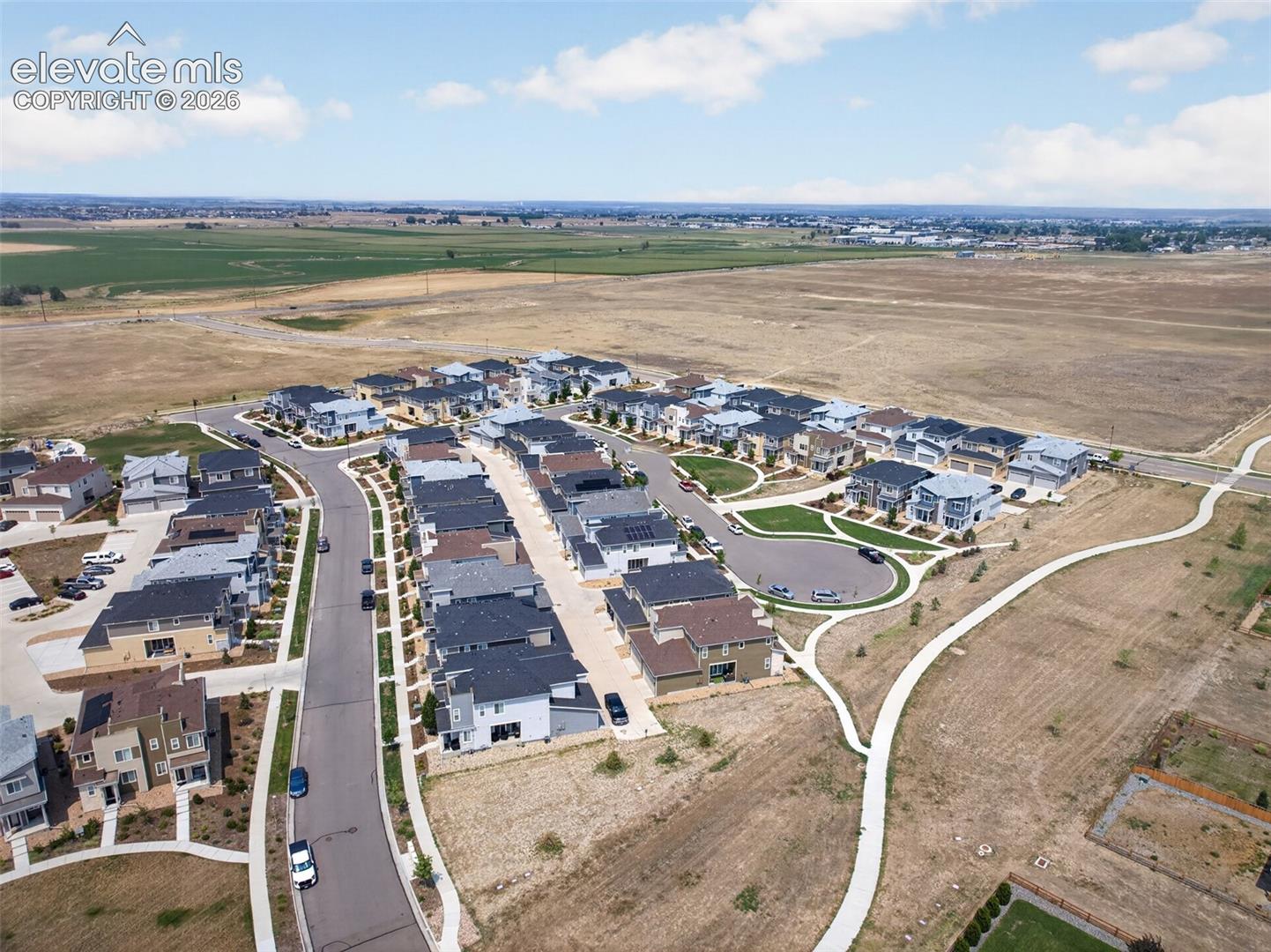 Aerial perspective of a planned residential development featuring paved concrete streets, concrete sidewalks, multi-level homes with pitched roofs, and extensive undeveloped open land