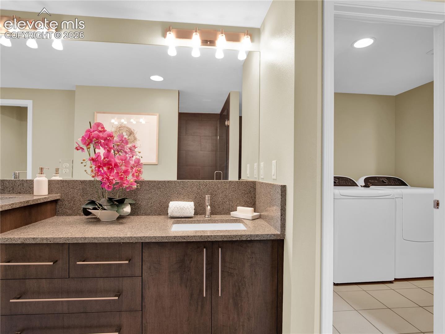 Wood-finish vanity cabinetry with brushed metal hardware, stone-surface countertop, rectangular under-mount sink, and dual light fixtures