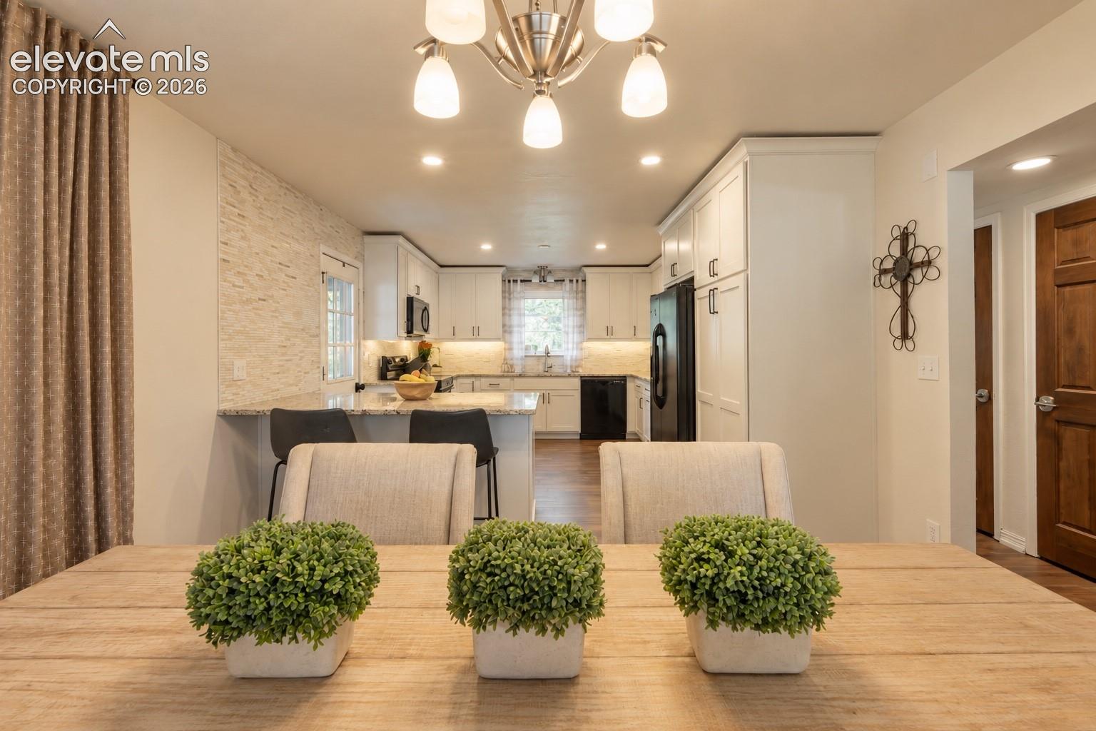 Open-concept kitchen featuring white cabinetry, black appliances, recessed lighting, and a breakfast bar with granite-style countertops