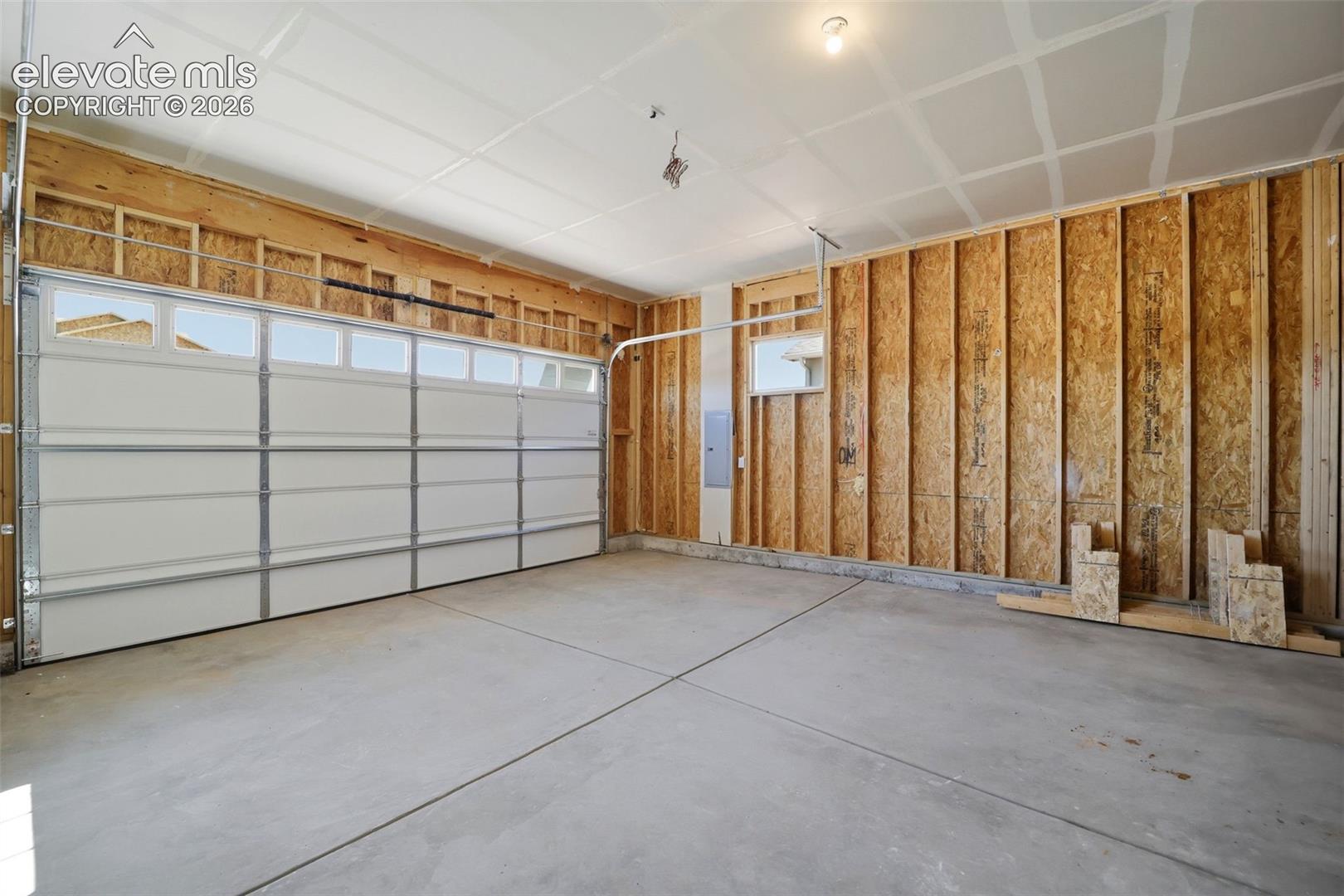 Multi-bay garage featuring concrete flooring, an overhead sectional door with transom windows, and exposed wood-frame wall construction