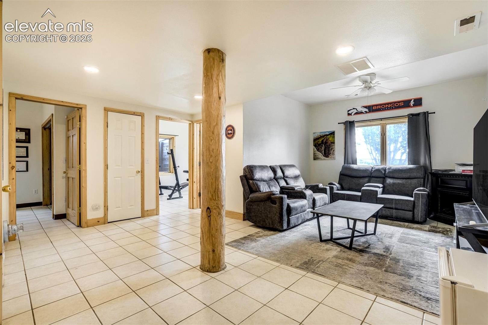 Spacious room featuring light-colored tile flooring, multiple doorways with wood trim, and a prominent wood-finish support column