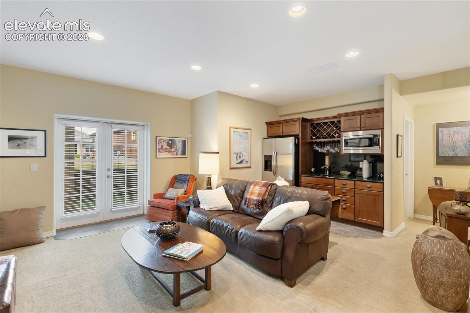 Living area featuring recessed lighting, a built-in wet bar with wood cabinetry, stainless steel appliances, a wine rack, and a double-door exterior entry