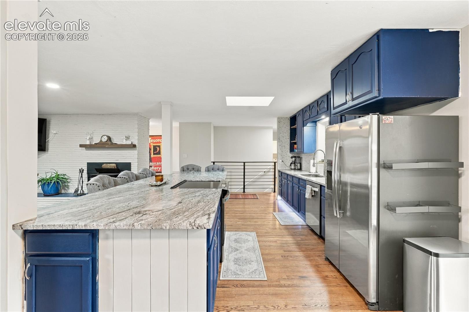 Kitchen featuring a sprawling stone-surface island, blue custom cabinetry, stainless steel appliances, wood-finish flooring, and a skylight