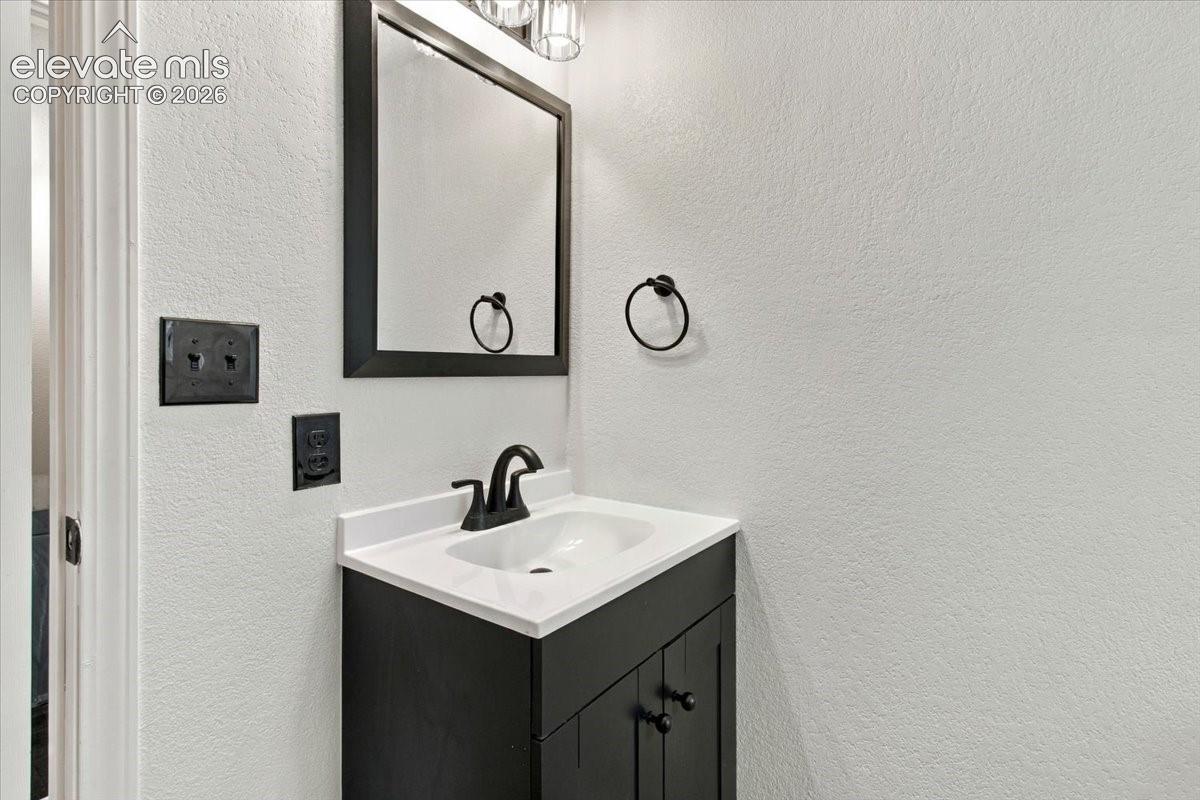 Black vanity with a white countertop and drop-in basin, matte black faucet, framed mirror, and coordinating matte black towel ring