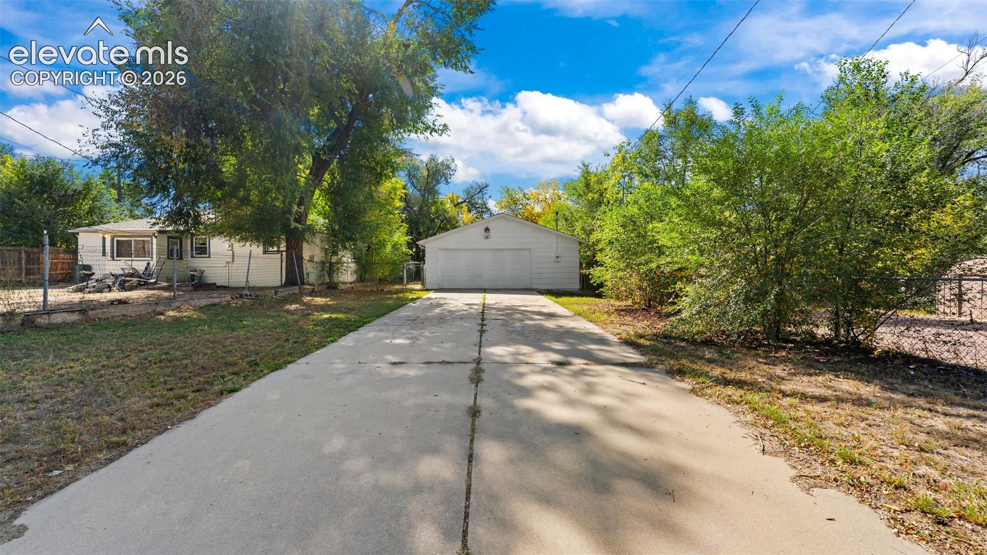 Detached garage with two garage doors, extensive paved driveway, and mature landscaping
