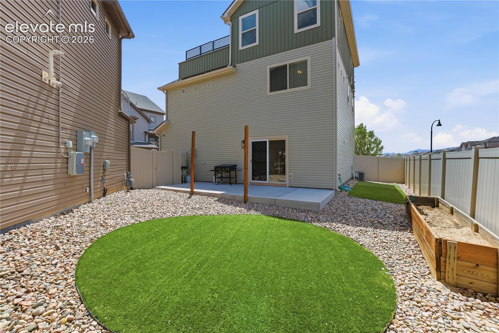 Rear exterior with a concrete patio, sliding glass door, and a circular artificial turf area