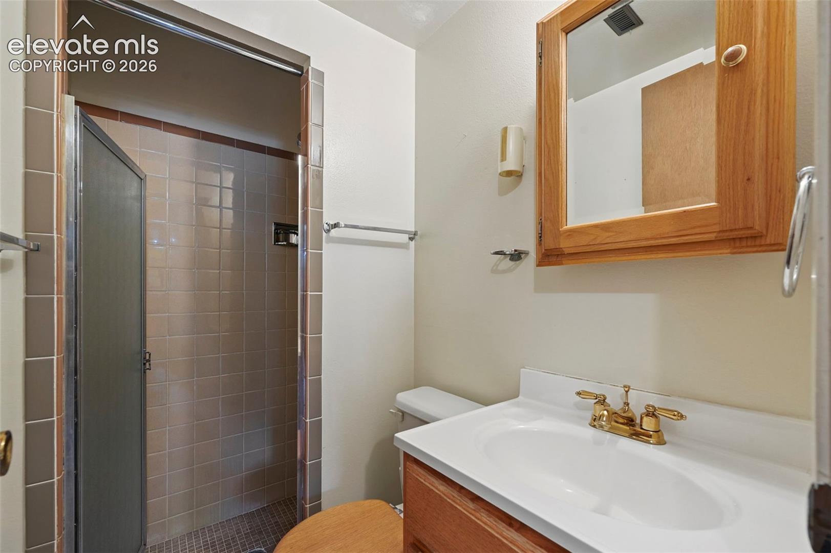 Bathroom featuring a vanity with integrated sink, brass-finish hardware, wood-frame medicine cabinet, and tiled shower enclosure with metal-framed glass door