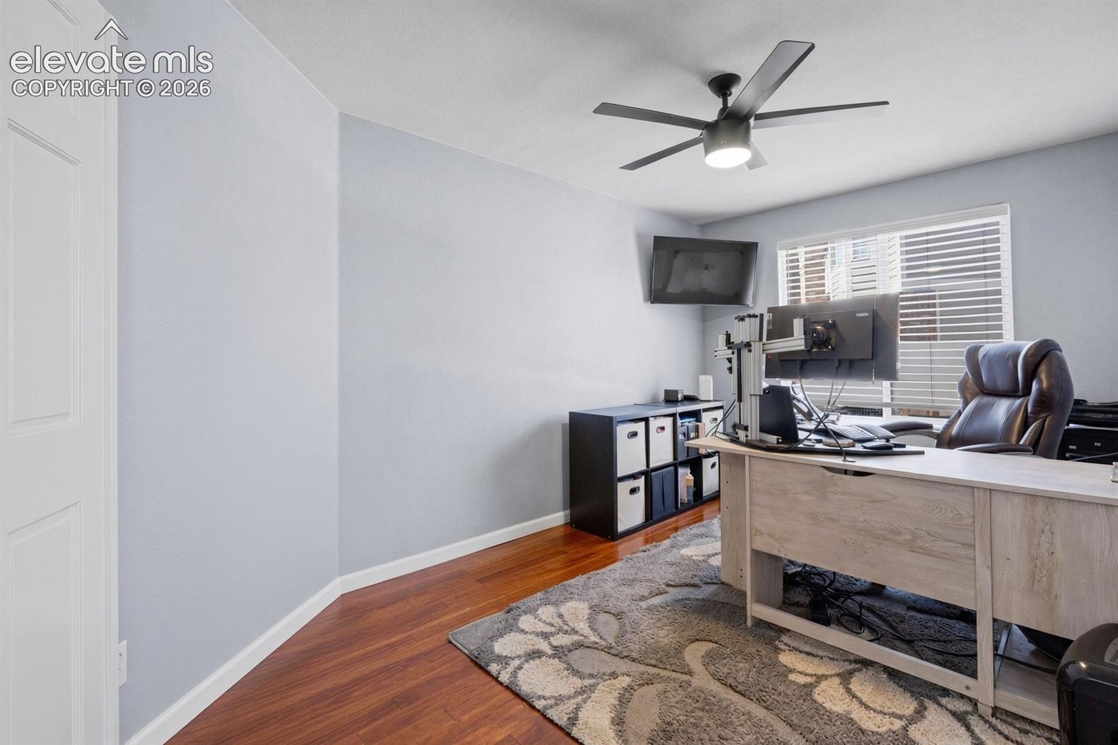 Room featuring wood-finish flooring, a multi-blade ceiling fan with integrated lighting, and horizontal window blinds