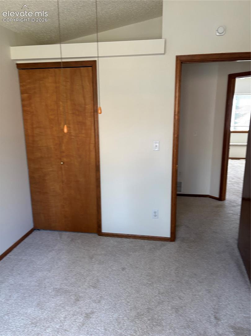 Vaulted ceiling, interior closet with wood-finish doors, and wood-trim door casing