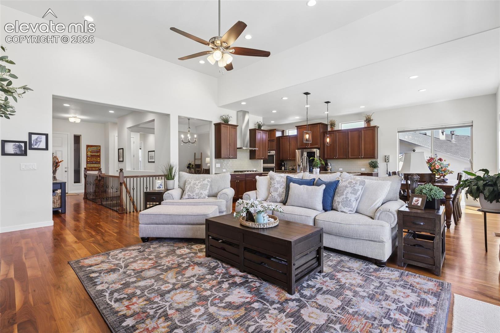 Vaulted ceiling with a ceiling fan, recessed lighting, wood-finish flooring, and a kitchen with wood cabinetry