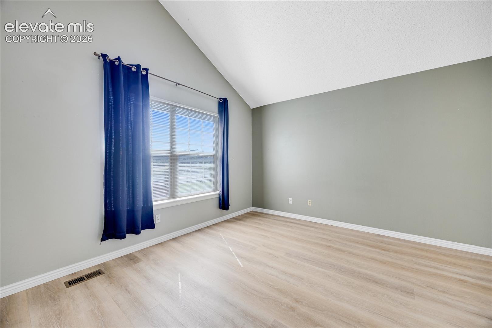 Vaulted ceiling, wood-finish flooring, broad window, and neutral wall tones
