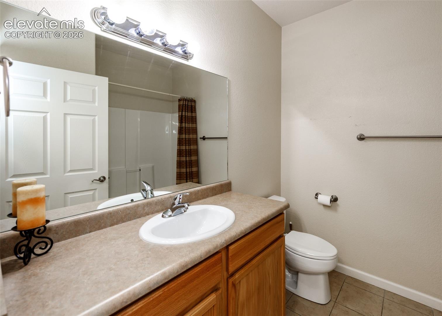 Bathroom featuring a wood vanity with a solid-surface countertop, an integrated oval sink, a wall-to-wall mirror, and overhead vanity lighting
