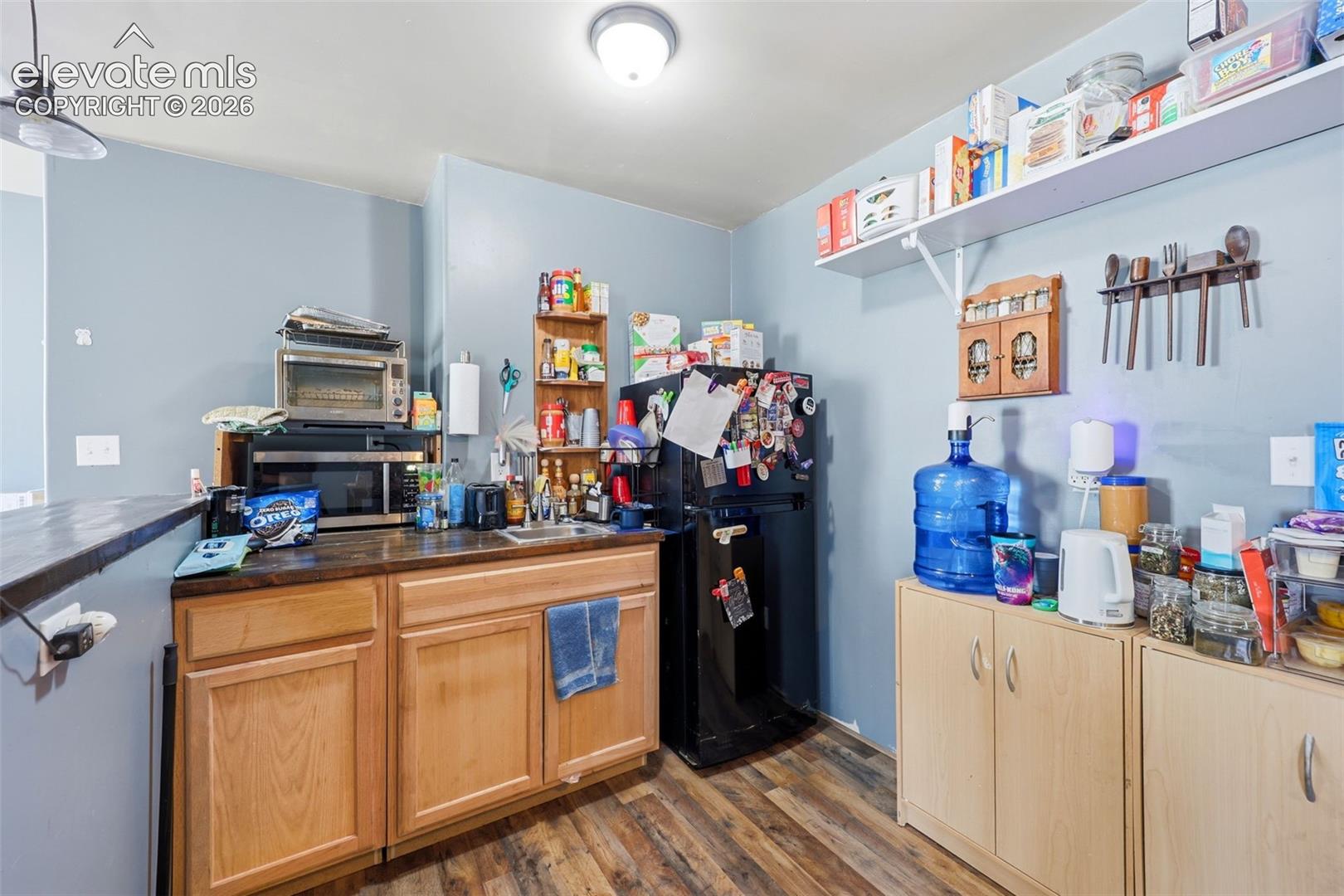 Kitchen area featuring wood-finish flooring, light blue walls, wood cabinetry, and a dark countertop