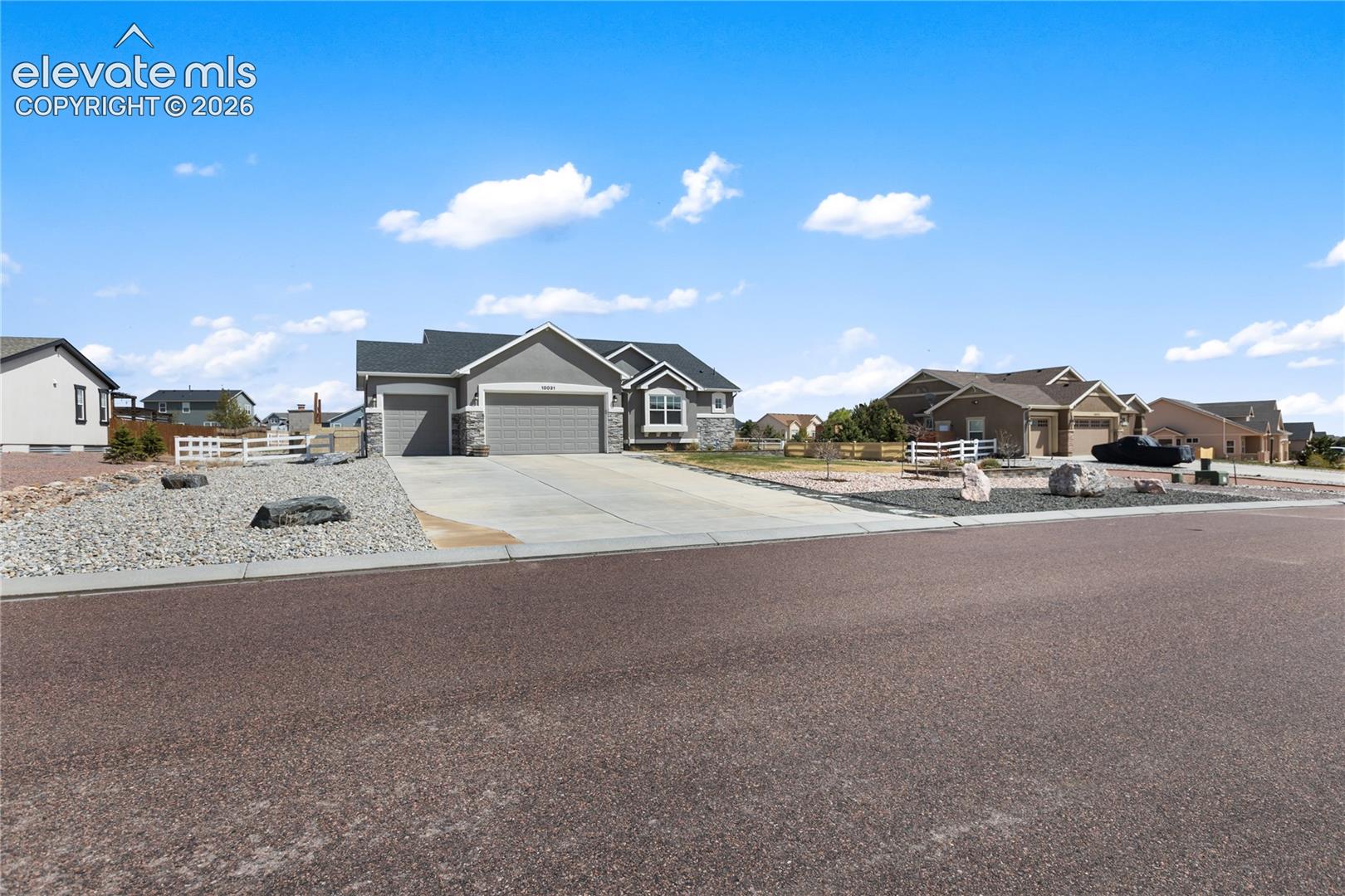 Ranch-style home featuring a gray facade with stone accents, an attached three-car garage, and a concrete driveway