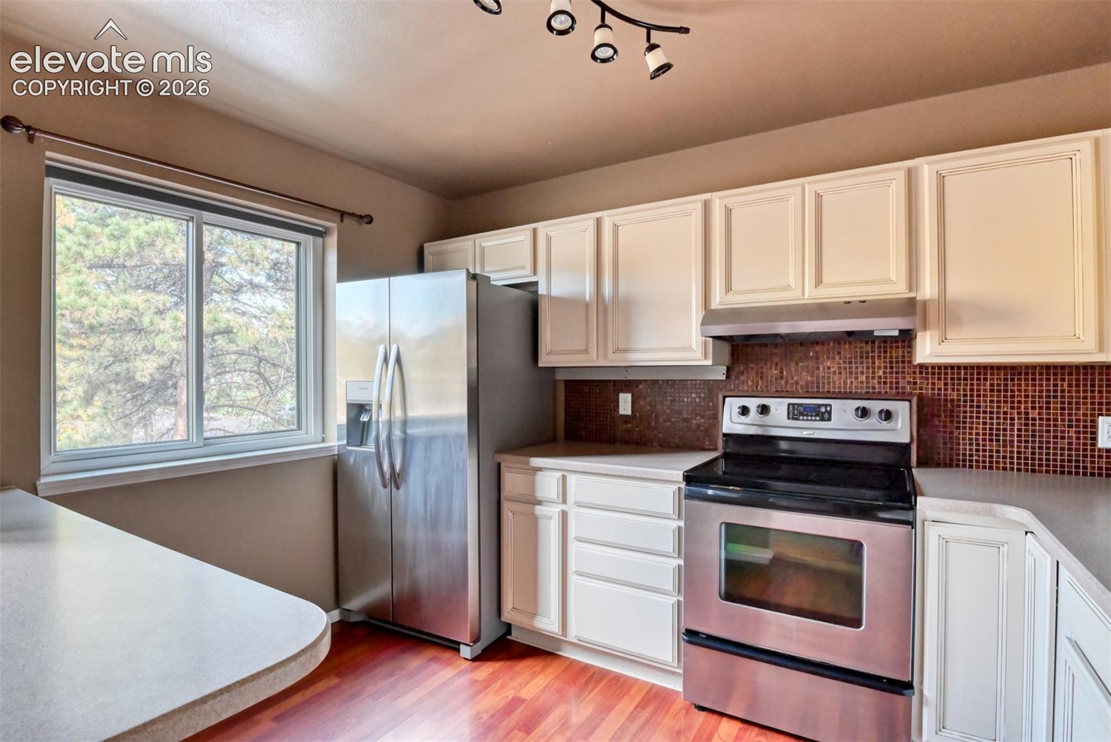 Kitchen featuring stainless steel appliances, a tile backsplash, white cabinetry, and wood-finish flooring