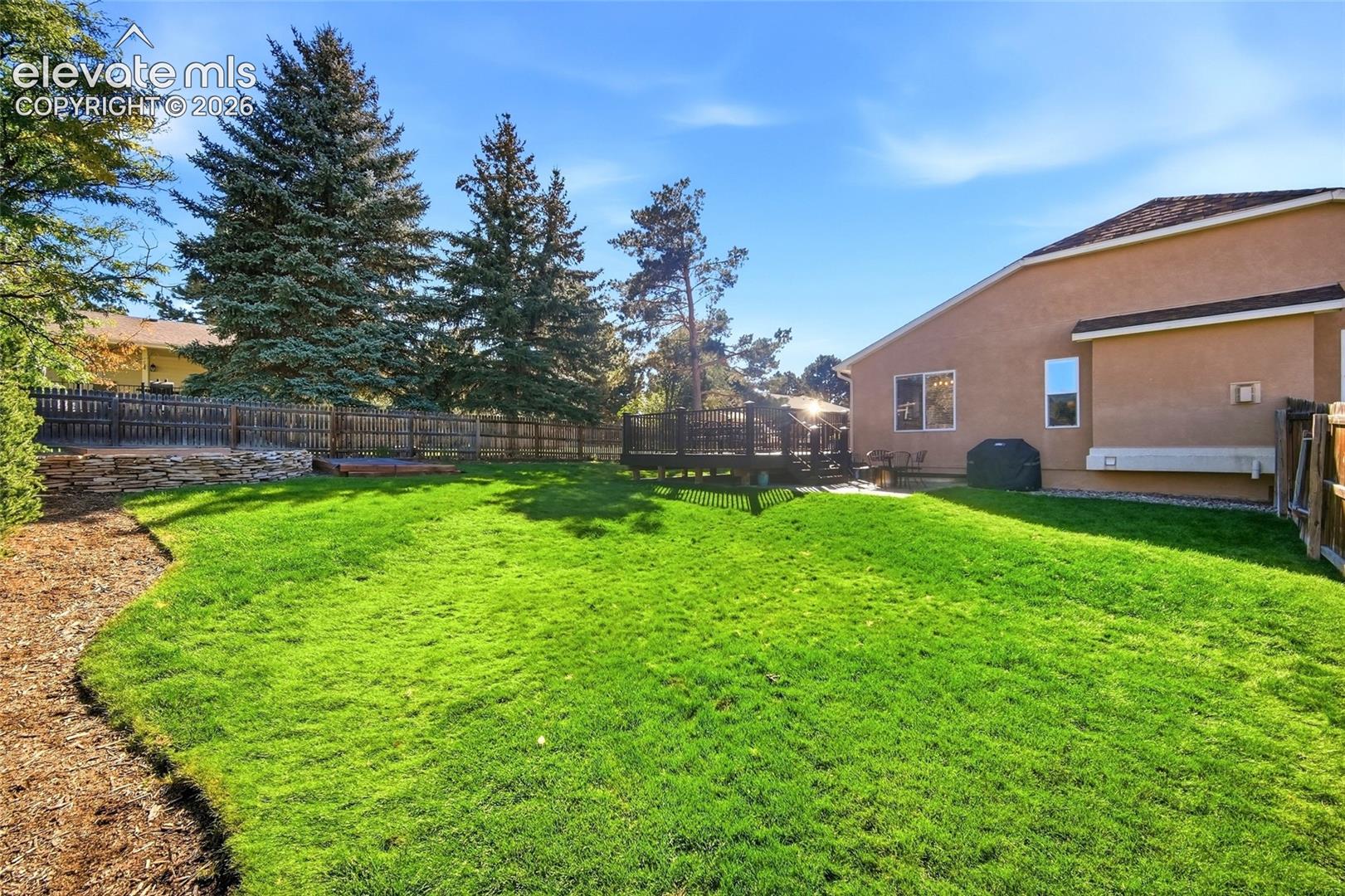 Expansive lawn area, wood privacy fencing, raised wood deck, stone retaining wall, and mature trees