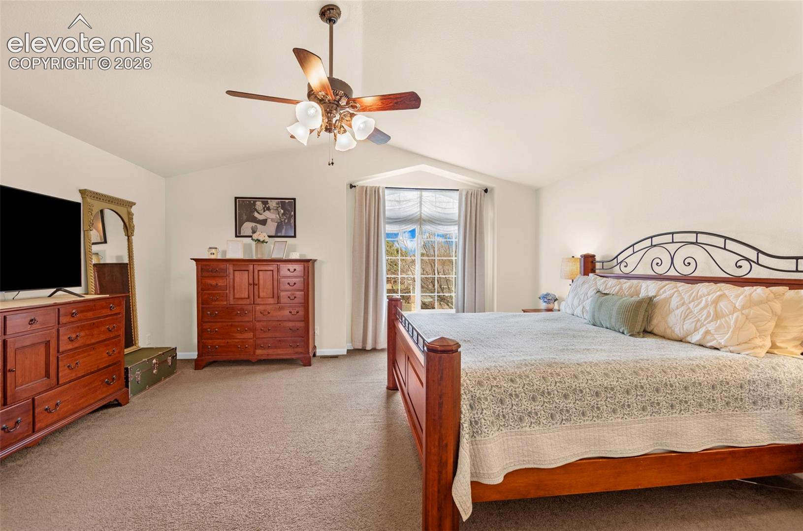 Vaulted ceiling bedroom with a prominent large window, soft neutral wall tones, and plush carpeting