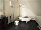 Clawfoot soaking tub with a wall-mounted shower ring, dark stone-finish flooring, and a dark-toned vanity cabinet