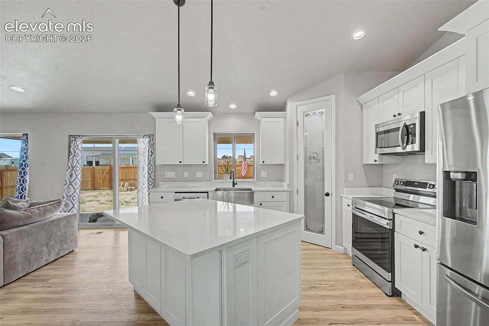 Modern kitchen featuring a large central island with a solid surface countertop, white shaker-style cabinetry, and stainless steel appliances including a refrigerator, microwave, and range
