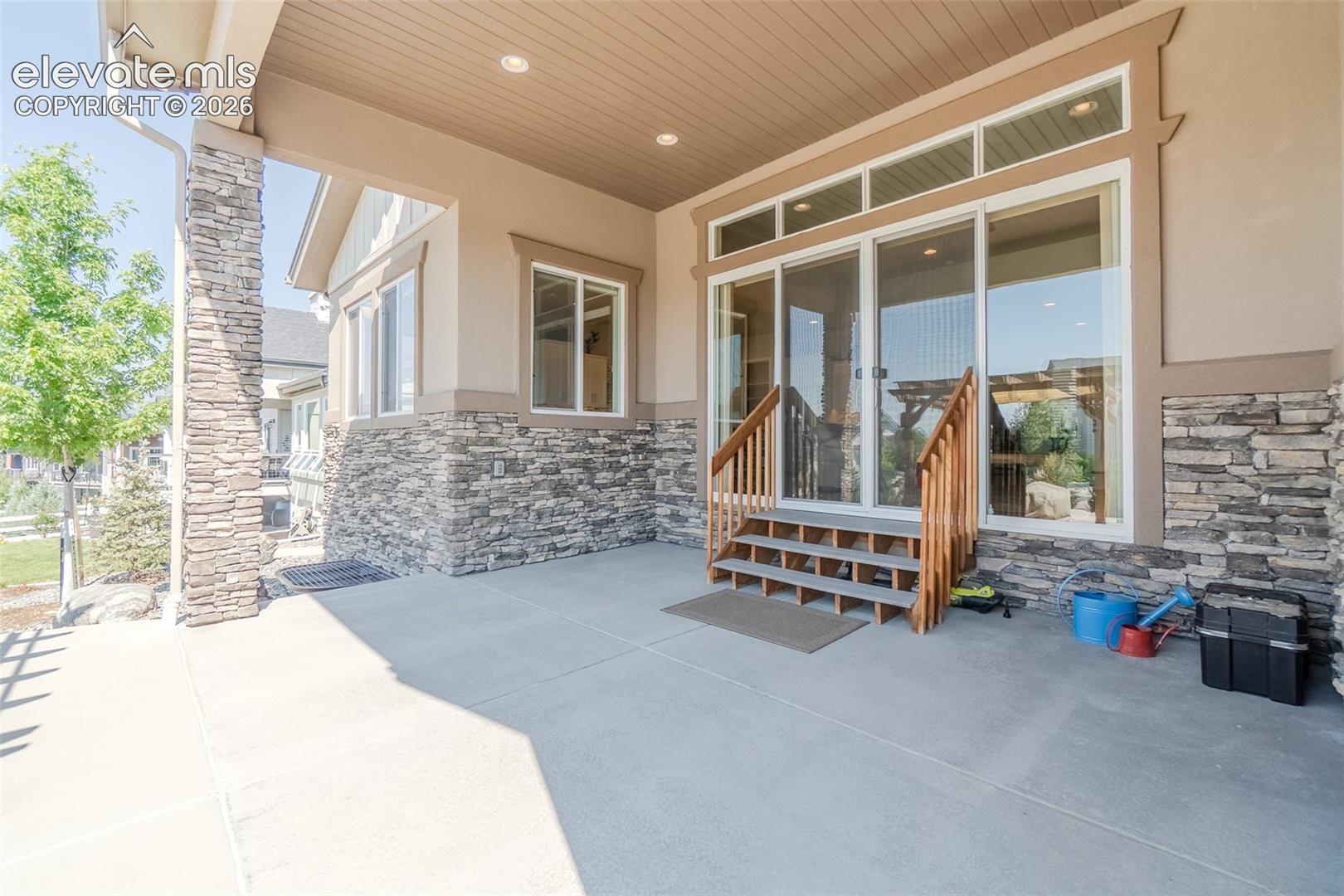 Covered patio featuring stone veneer accents, concrete flooring, recessed lighting, and a sliding glass door entry with wood stairs and railings