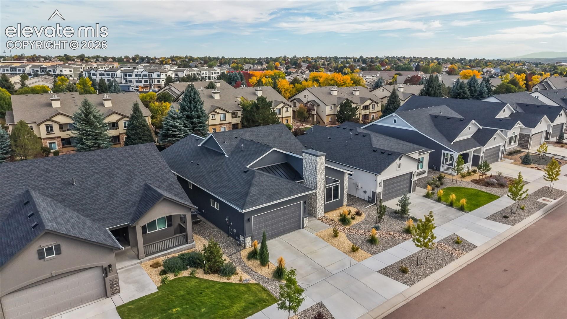 Aerial perspective of residential exteriors featuring multi-pitch shingled roofing, stone masonry accents, multi-car garages, and concrete driveways