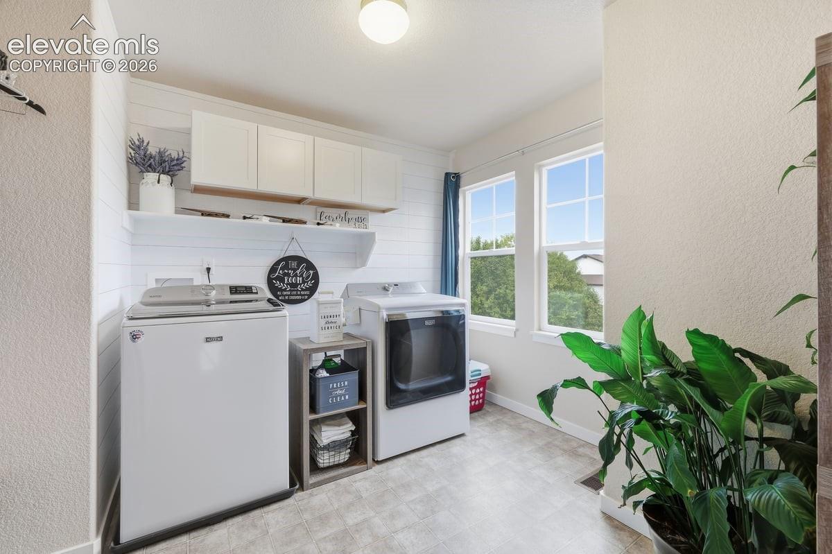 upstairs laundry room with accent shiplap wall and upper cabinets for storage