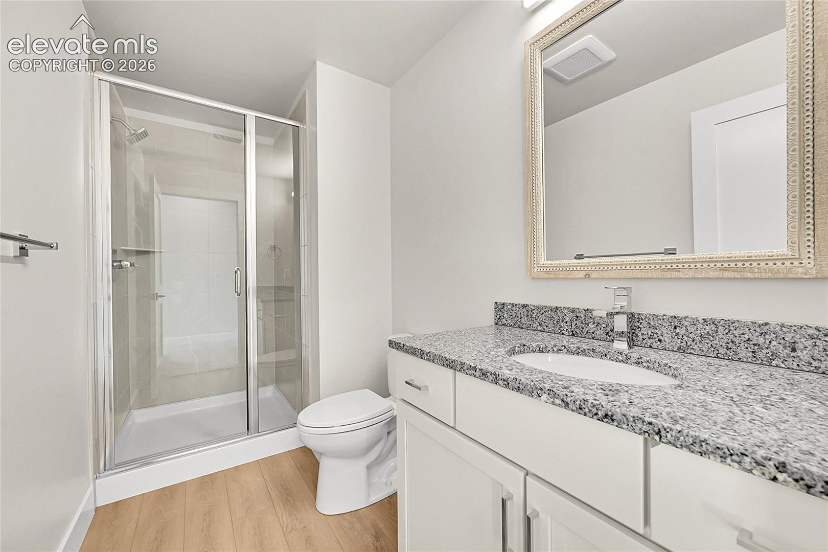 Bathroom featuring a frameless glass shower enclosure, a white ceramic toilet, and a vanity with a speckled countertop