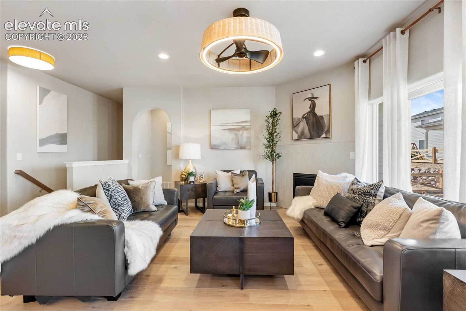 Living area featuring wood-finish flooring, a drum-style ceiling fan with integrated lighting, an arched wall opening, recessed lighting, and large windows with floor-to-ceiling drapery hardware