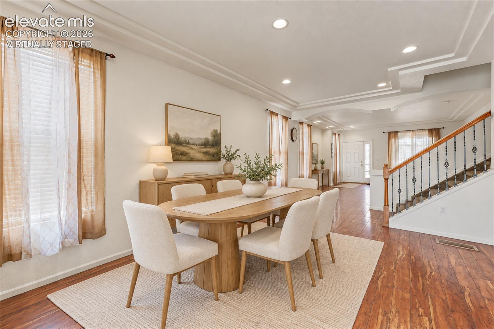 Virtually Staged Open-concept interior featuring wood-finish flooring, recessed lighting, double-tier tray ceilings, and a staircase with decorative metal balusters