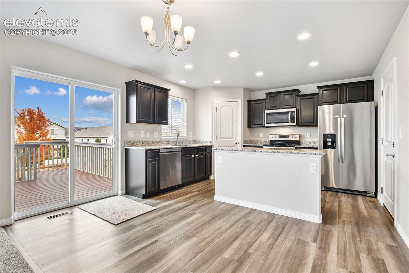 Kitchen featuring dark cabinetry, stone-surface countertops, stainless steel appliances, wood-finish flooring, and sliding glass doors to the exterior deck