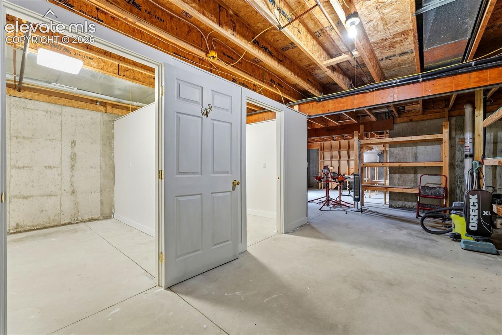 Unfinished lower level with concrete flooring, exposed wood beam ceiling, and separate framed rooms