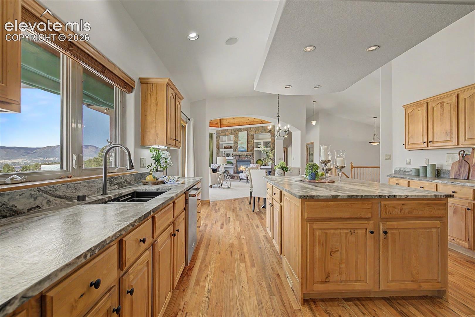 Spacious kitchen featuring light wood cabinetry, stone countertops, a large center island, and wood-finish flooring