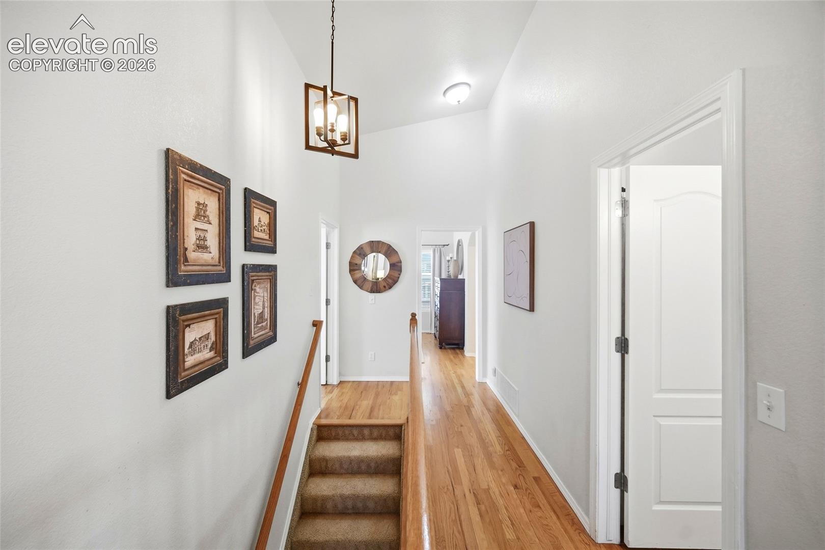 Vaulted ceiling, wood-finish flooring, staircase with carpeted treads, wood handrail, and a hanging light fixture