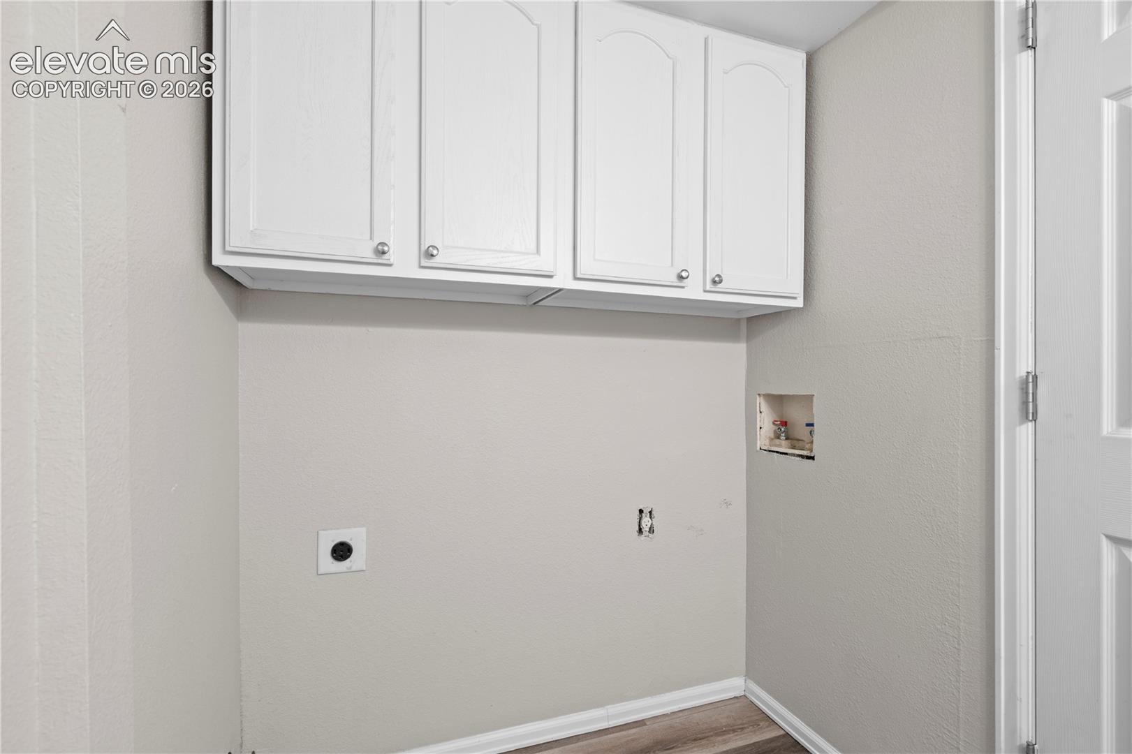 Wall-mounted white cabinetry featuring shaker-style doors with polished nickel hardware and wood-finish flooring