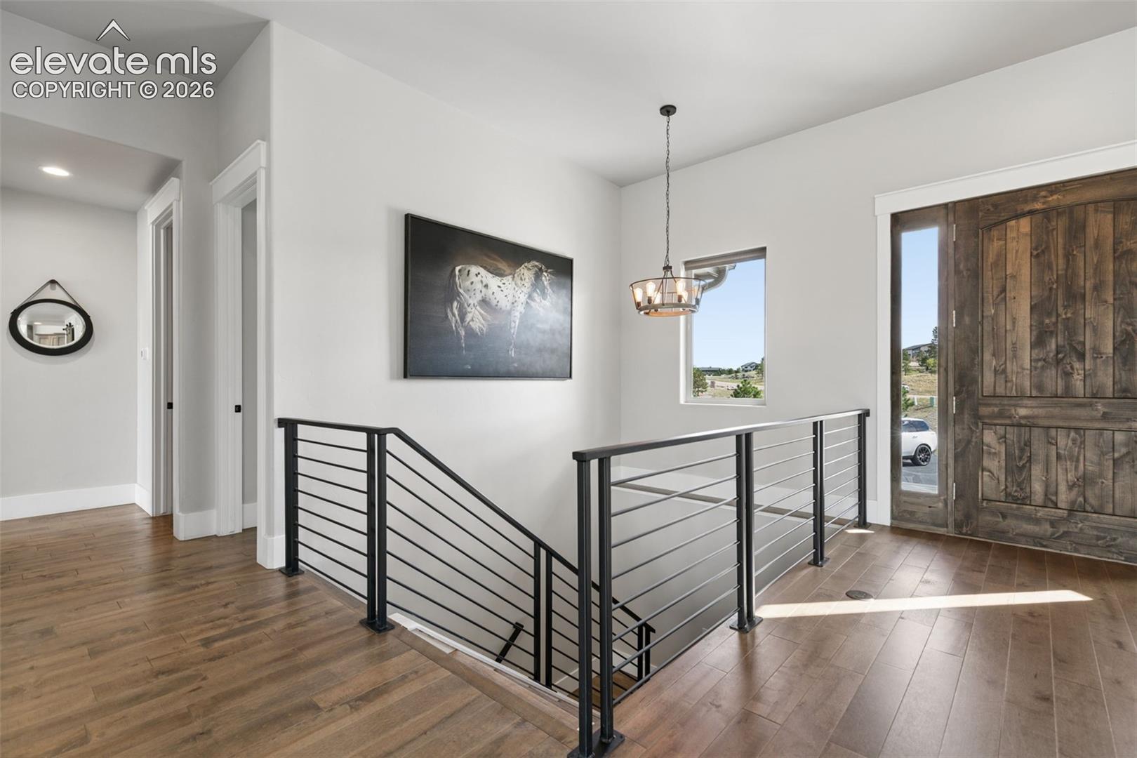 Rich wood-finish flooring, sleek horizontal metal railing, and a rustic wood plank entry door with a sidelight window