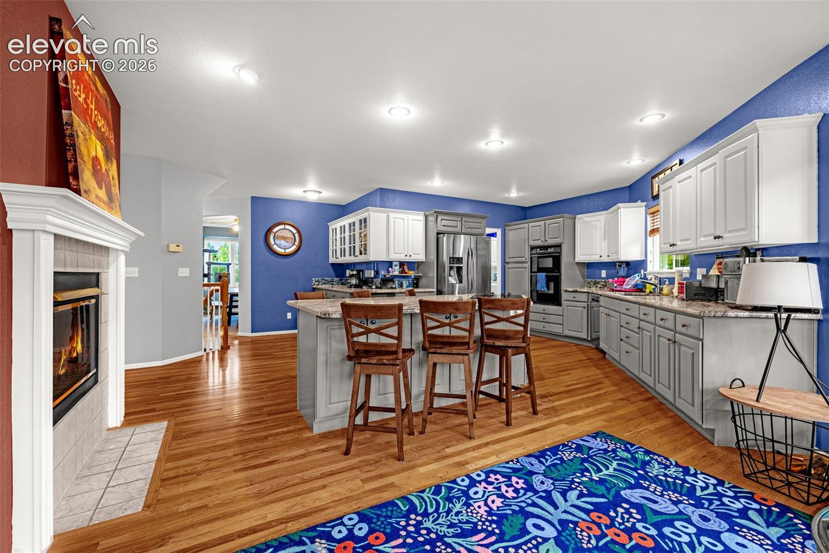 Open-concept living space featuring wood-finish flooring, a contemporary fireplace with tile surround, recessed lighting, and a kitchen island with seating