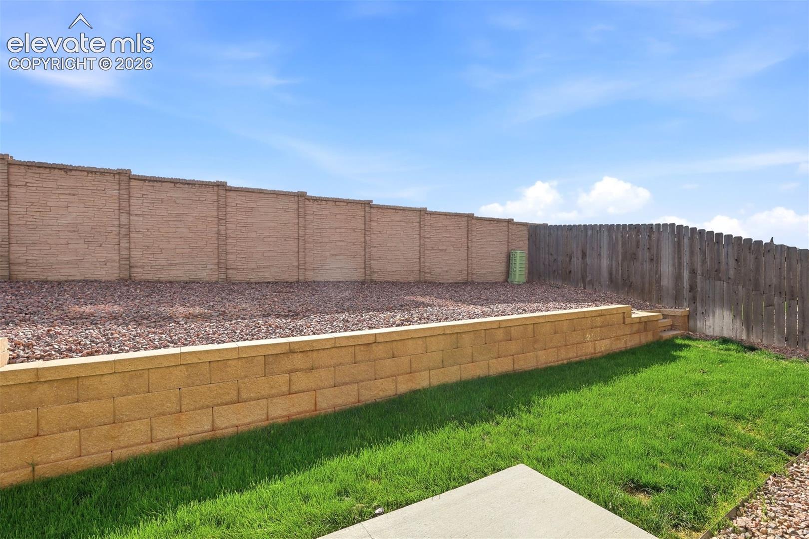 Tiered backyard landscaping featuring a block retaining wall, a full privacy fence, and a gravel-filled upper level