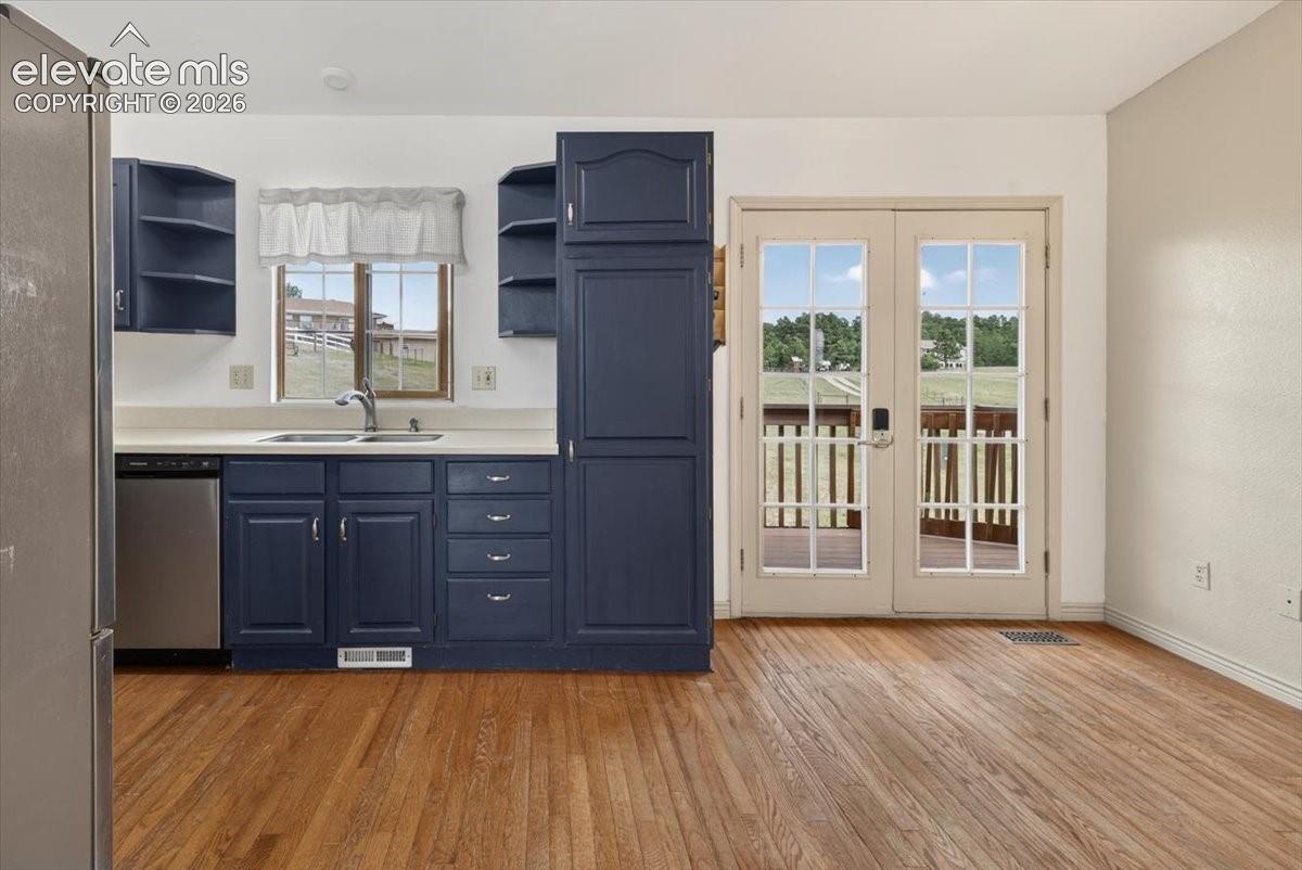 Kitchen featuring navy blue cabinetry, wood-finish flooring, dual-basin stainless steel sink, and French doors leading to exterior deck