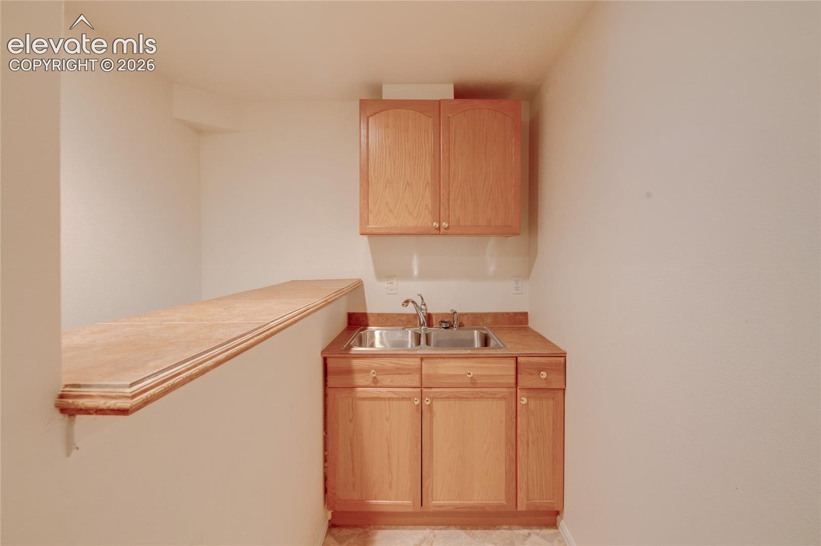 Kitchenette featuring light wood-finish cabinetry, a dual basin stainless steel sink, and a laminate countertop
