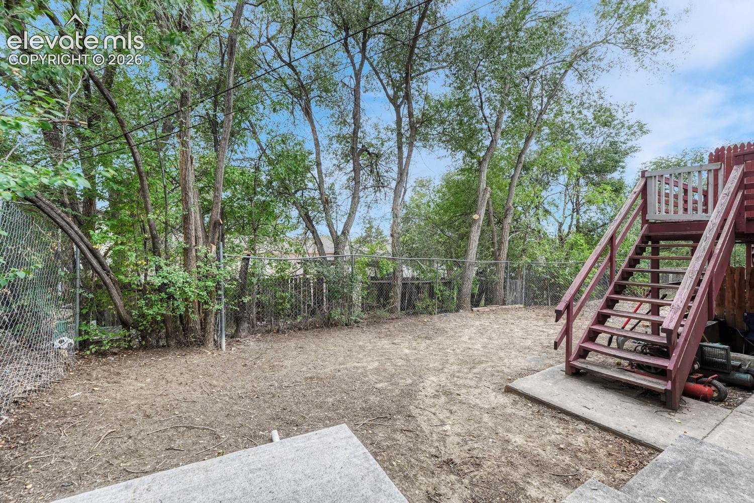 Expansive yard with mature trees, chain link fencing, a multi-level wood deck, and concrete patio