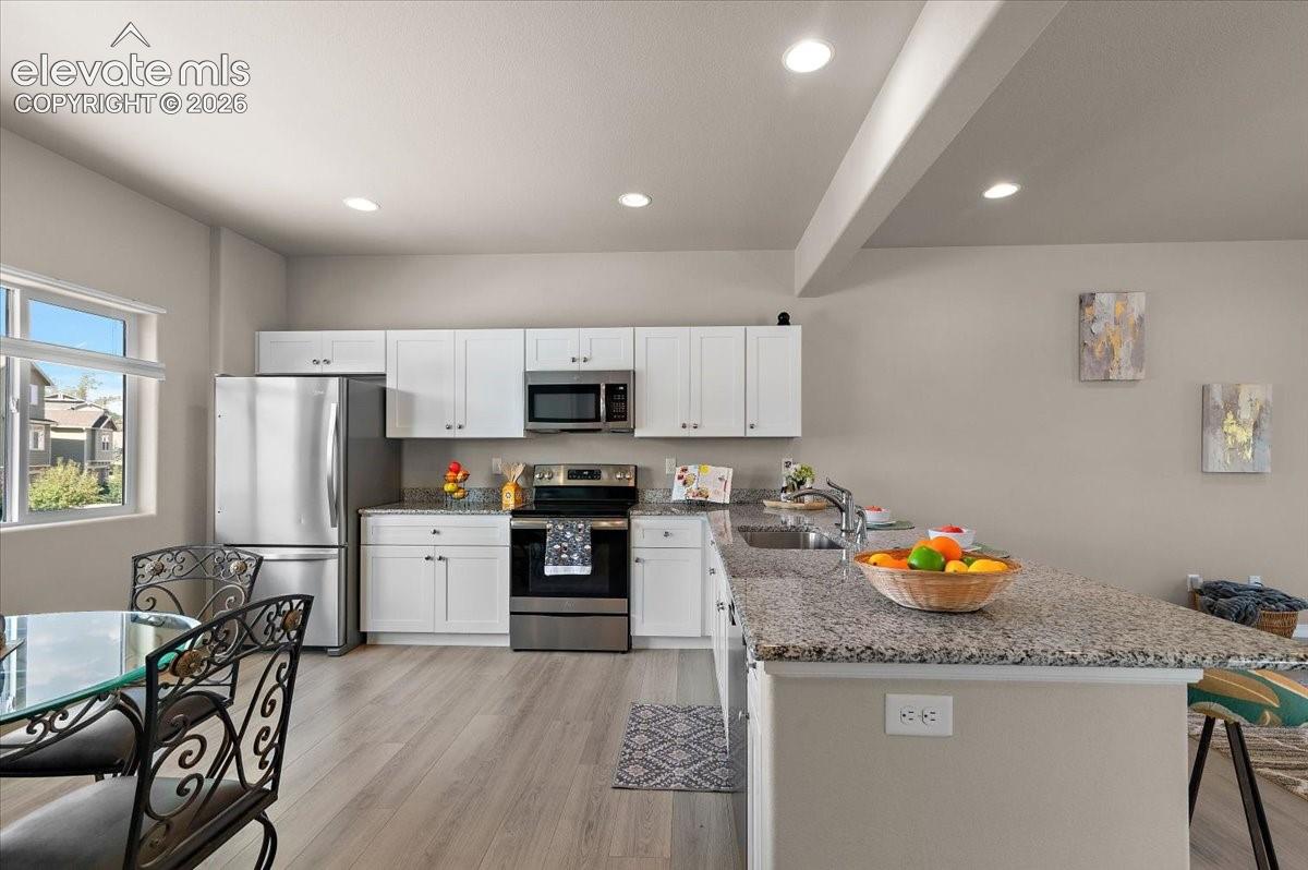 Kitchen featuring wood-finish flooring, white cabinetry, stainless steel appliances, and a granite-style island