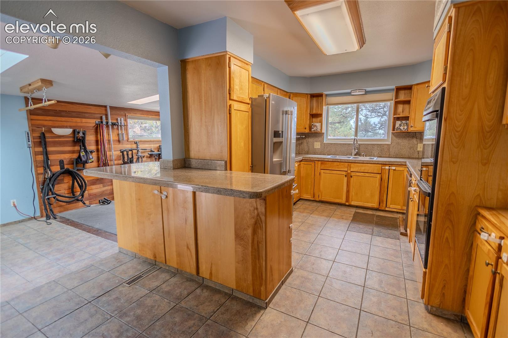 Kitchen featuring wooden cabinetry, stone-surface countertops, tile flooring, built-in wall oven, and stainless steel refrigerator